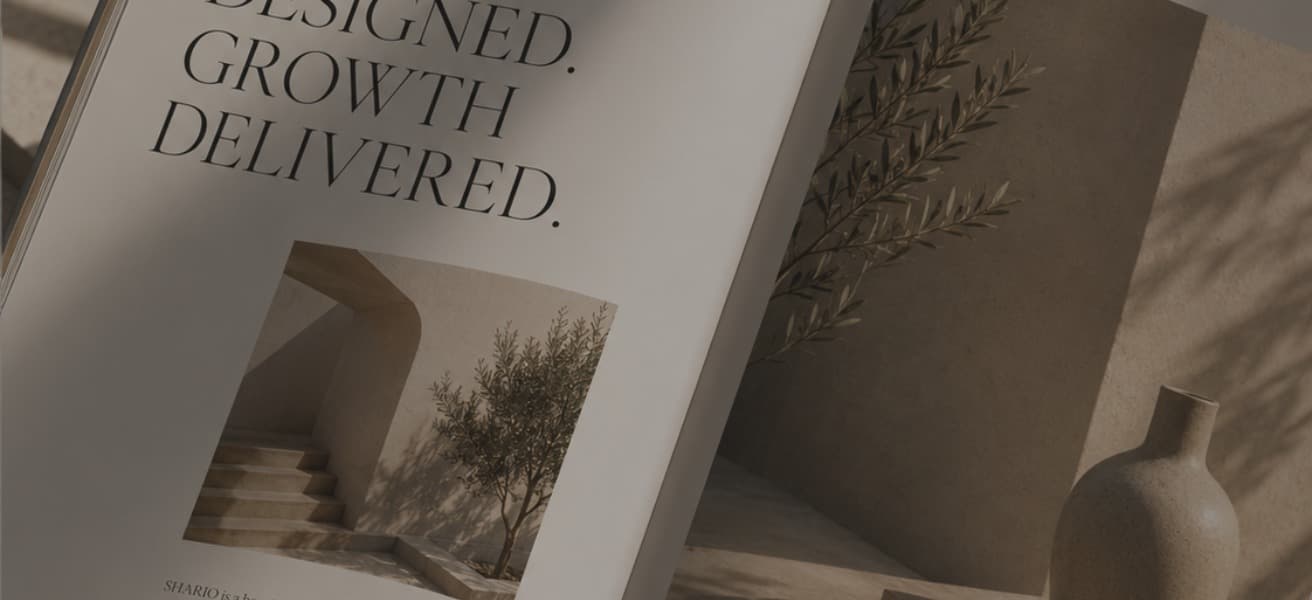 A softly lit editorial photograph of an open SHARIO brand lookbook, spread across a page reading 'Designed. Growth Delivered.' beside architectural and botanical brand imagery