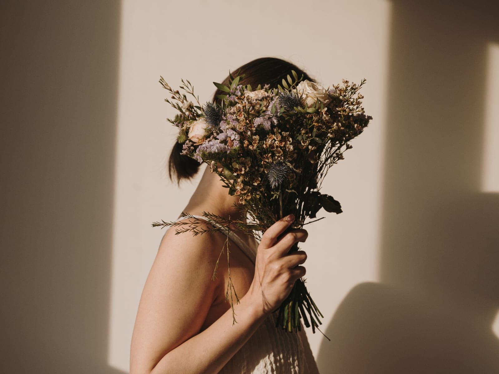 A woman holding a dried flower bouquet in front of her face, lit in warm sunlight